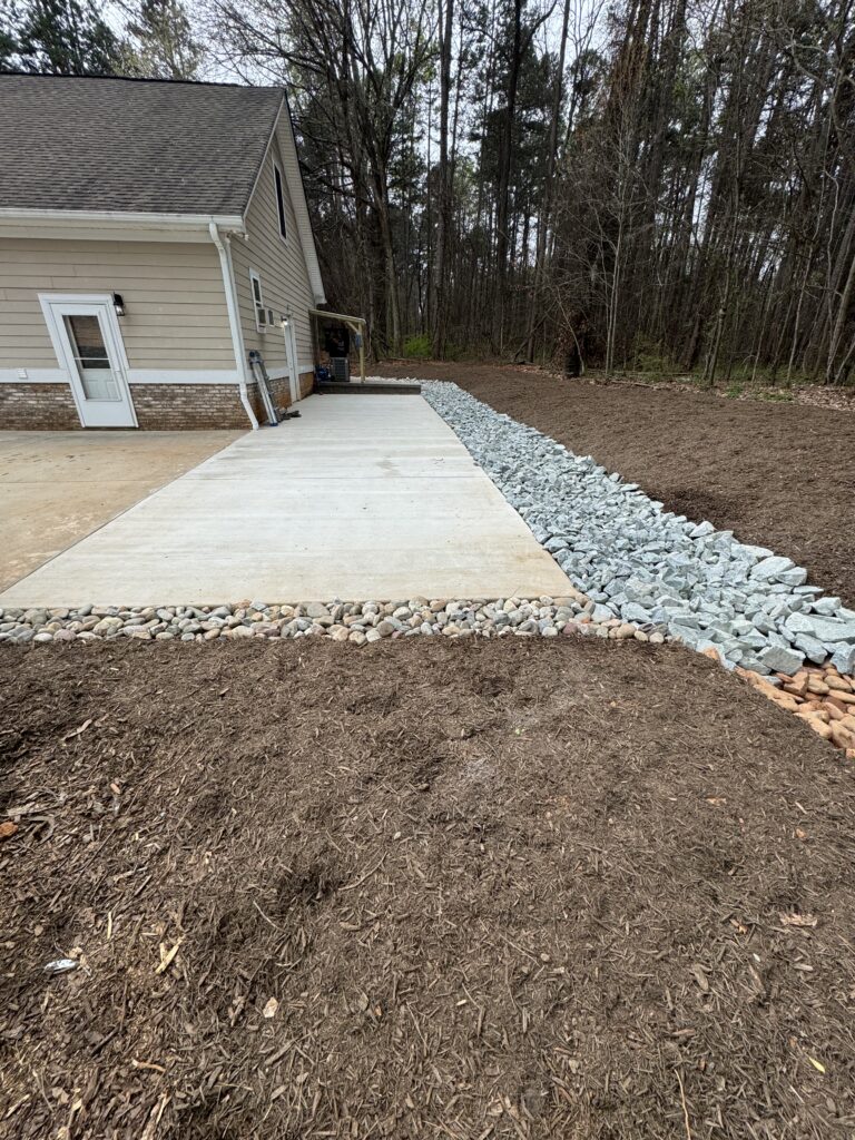 Stone-lined drainage area beside a concrete patio and house
