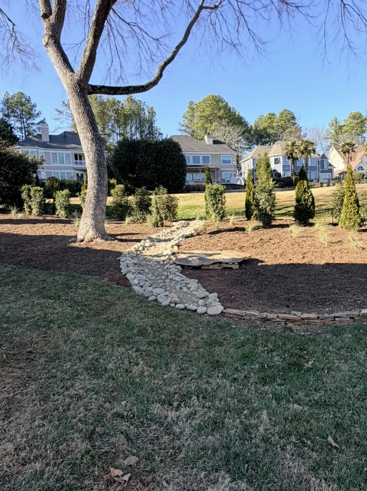 Stone-lined drainage swale through a landscaped front yard