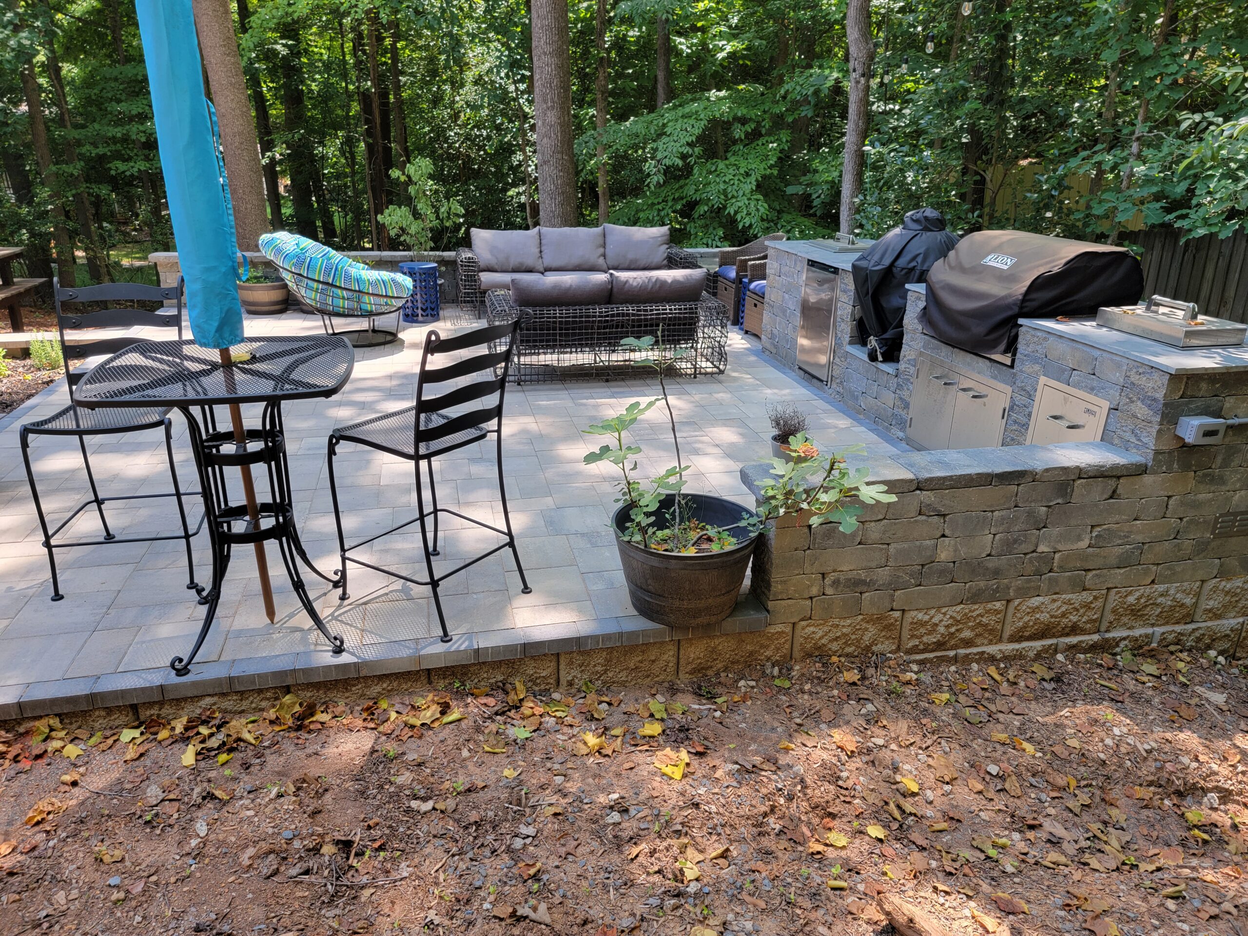 Outdoor kitchen with built-in grills beside a paver patio and dining area