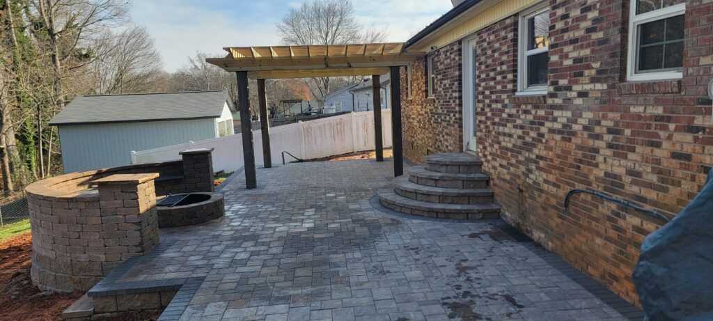 Paver patio with a pergola and curved steps beside a brick house