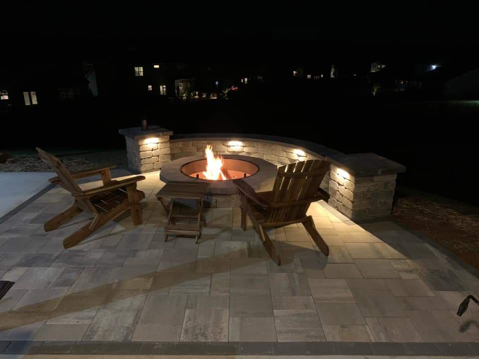 Paver patio with a fire pit and curved seating wall at night