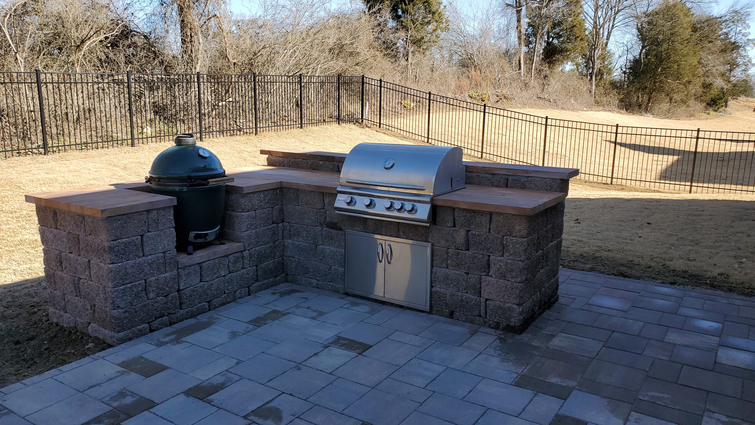 Outdoor kitchen with a built-in grill and ceramic cooker on a paver patio