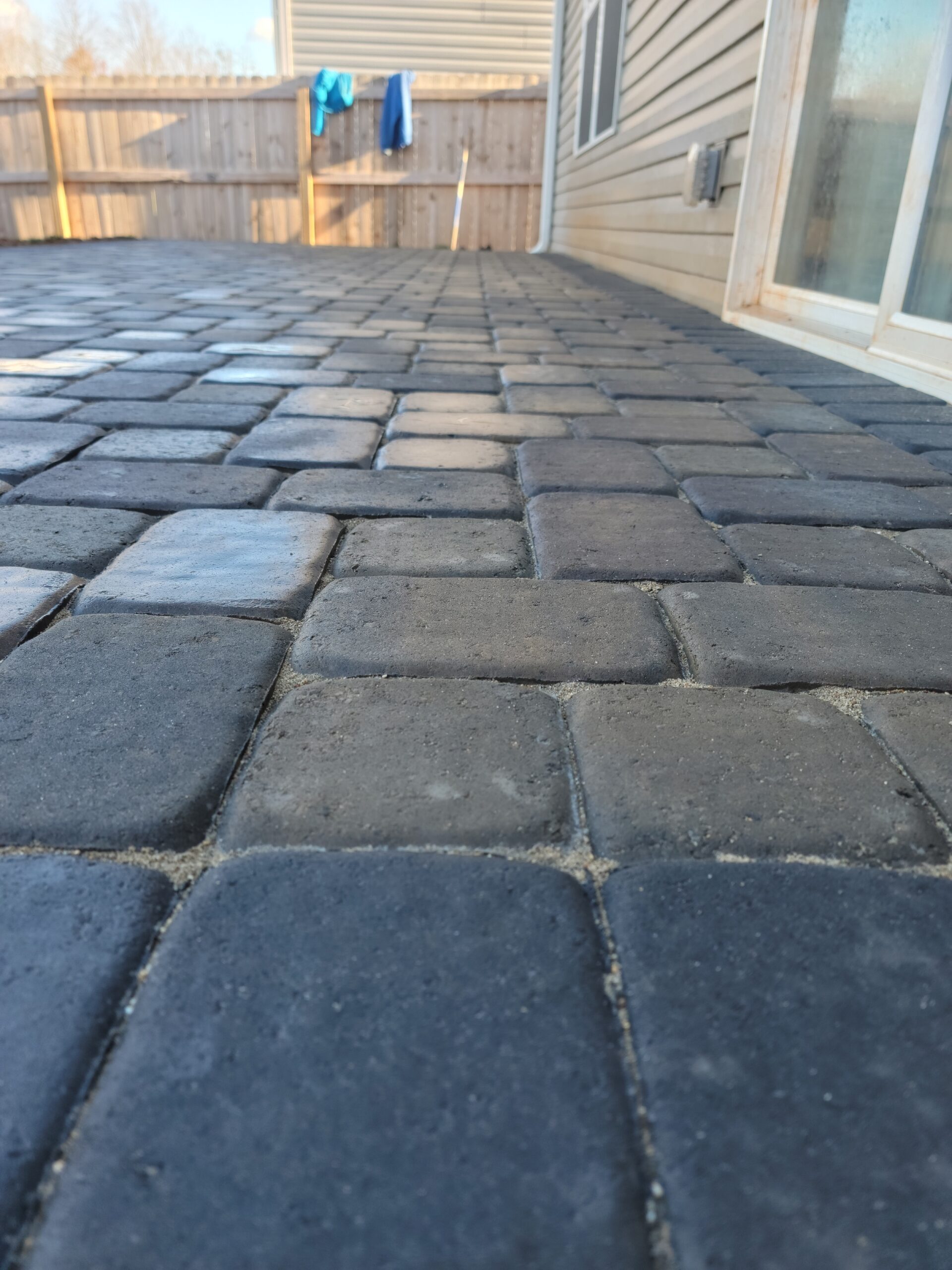 Gray paver patio beside a home and wooden privacy fence