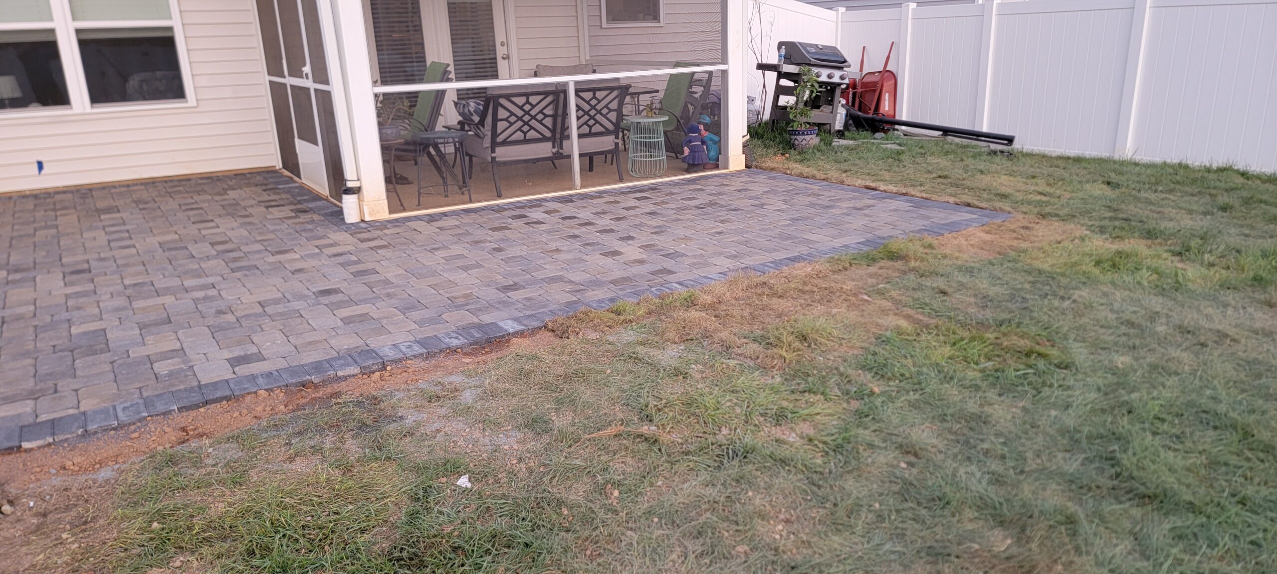 Finished gray paver patio and walkway beside a screened porch