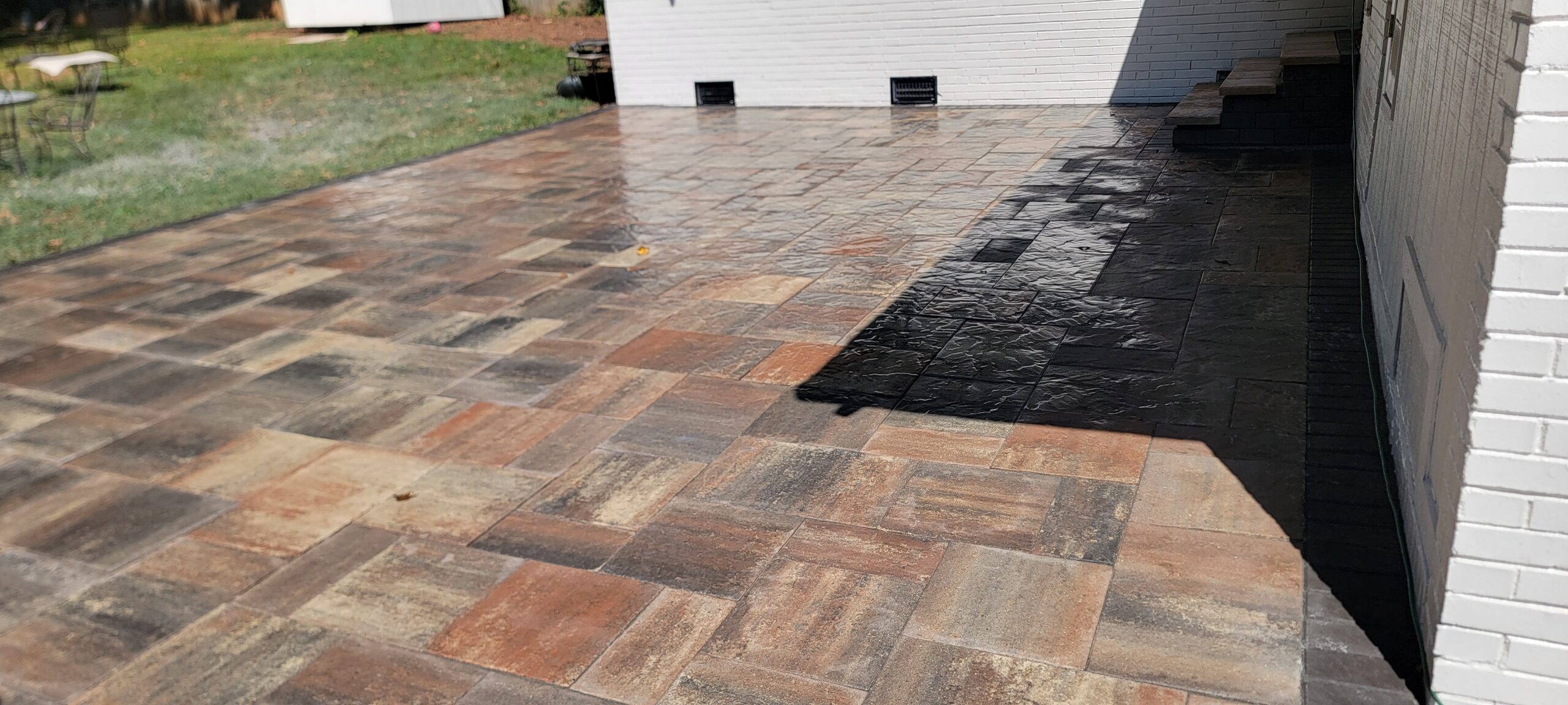 Multi-color paver patio installed beside a white brick home