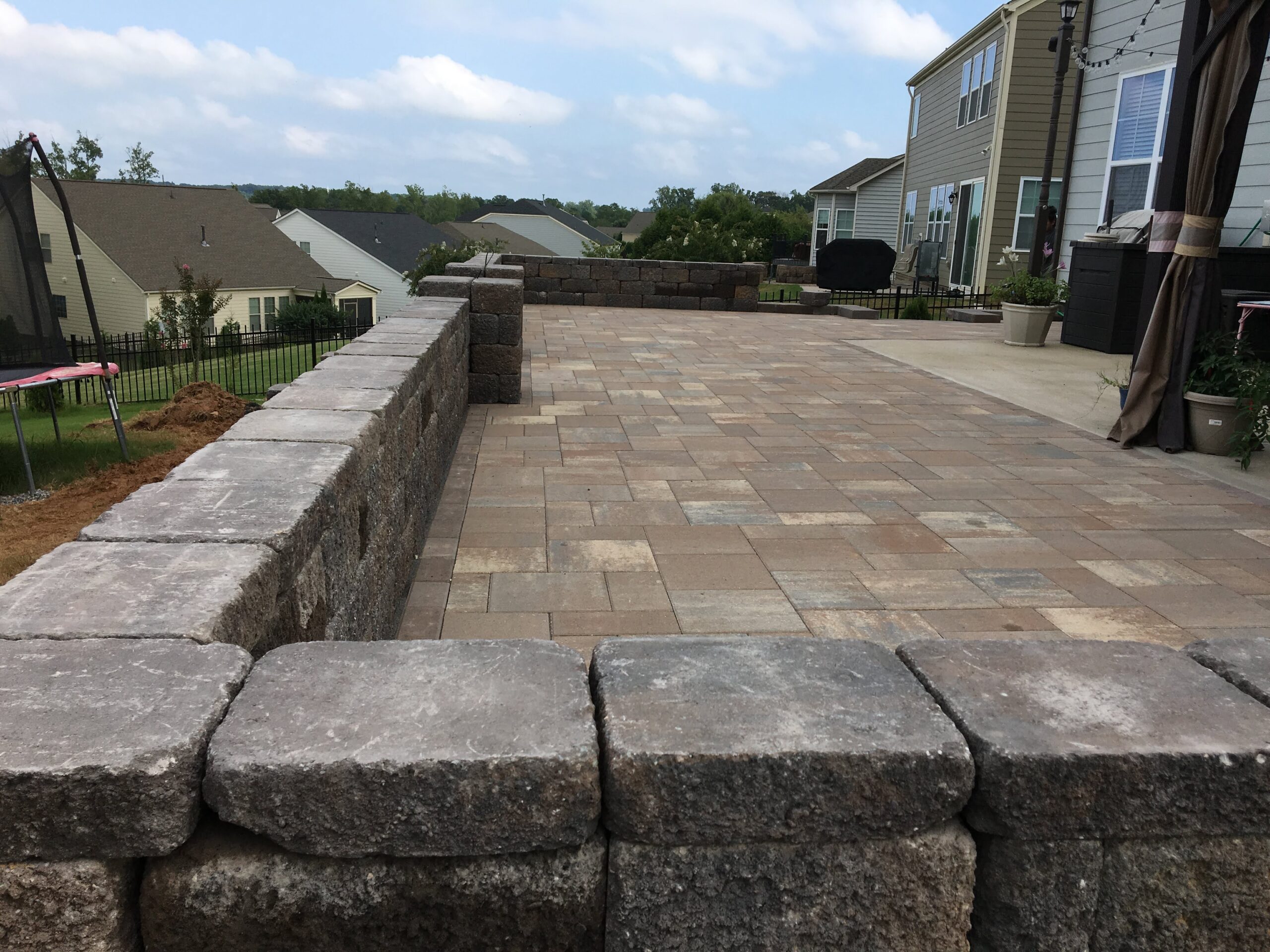 Large paver patio bordered by a block retaining wall