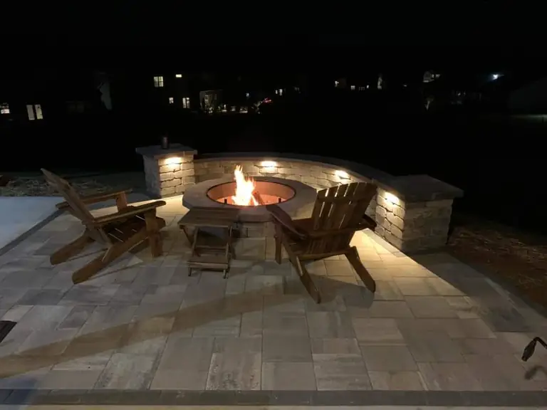 Paver patio with a fire pit and curved seating wall at night